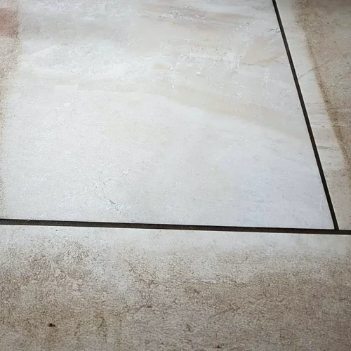 Beige porcelain floor tiles with dirty grout lines beside a freshly cleaned test area